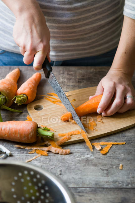 Midsection da mulher que corta a cenoura na placa de madeira — Fotografia de Stock