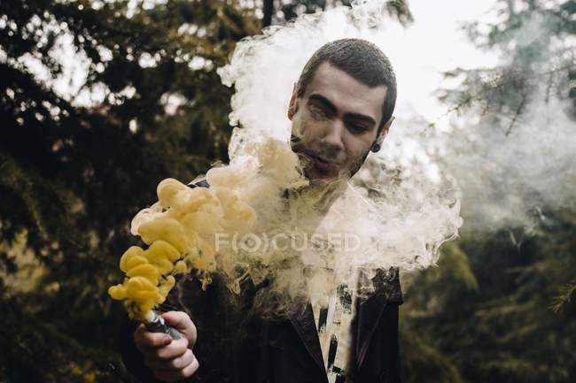 Portrait of young man looking at smoke candle in hand among woods — Stock Photo