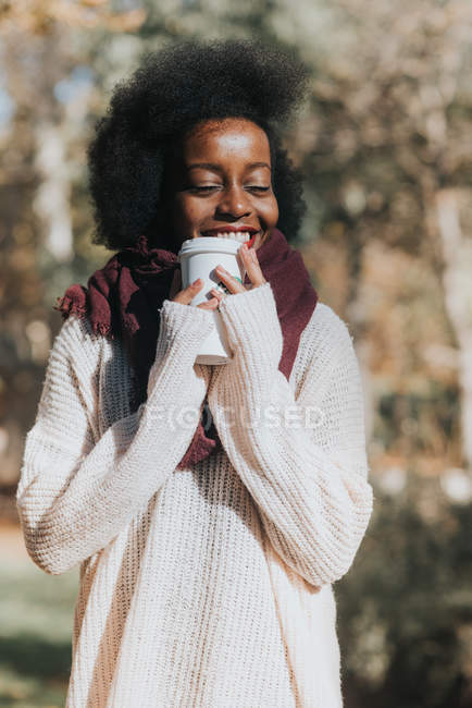Портрет счастливой девушки, держащей чашку кофе у лица и позирующей с закрытыми глазами в осеннем парке — стоковое фото