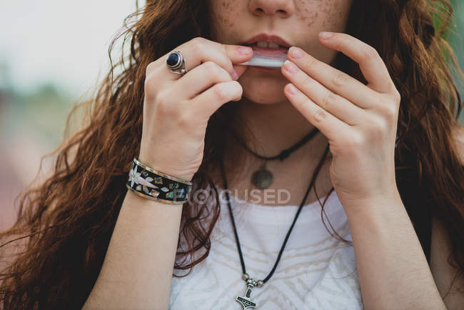 Cropped view of female licking cigarette paper to roll up joint — Stock Photo