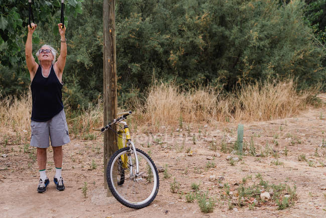 Vista frontale di senior facendo power-up vicino alla bicicletta in campagna — Foto stock