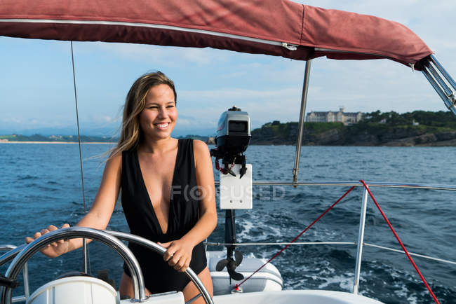 Portrait of smiling blonde girl in swimsuit posing at helm on yacht deck — Stock Photo