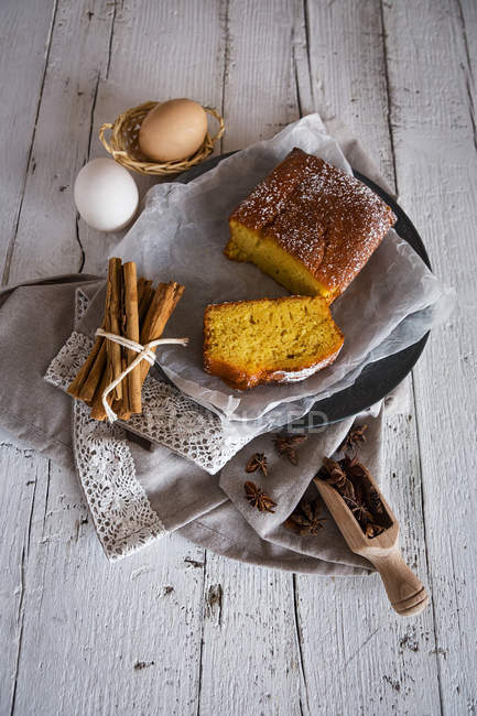 Высокий угол обзора лимонного торта с ингредиентами на хлебобулочной бумаге над белым сельским столом — стоковое фото