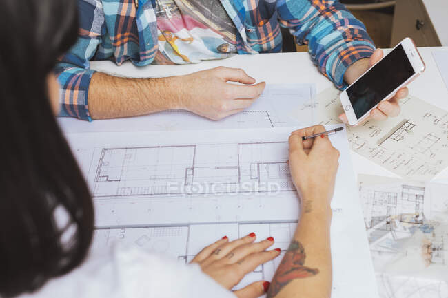 Male hands showing smartphone screen over blueprints while woman sketching — Stock Photo