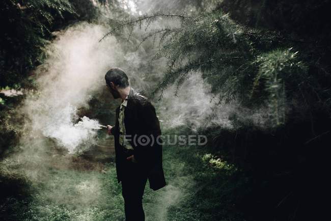 Портрет молодого чоловіка, що стоїть серед лісу і дивиться на дим свічки в руці — стокове фото
