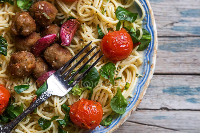 Sopra vista di forchetta su piatto pieno di pasta con polpette e pomodorini su tavolo rustico in legno — Foto stock