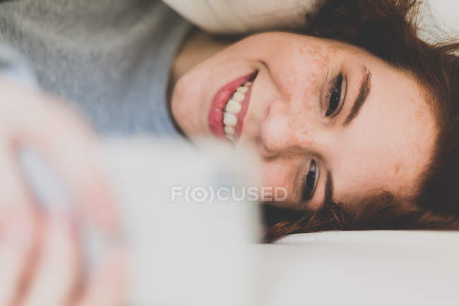 Girl lying in bed and using smartphone — Stock Photo