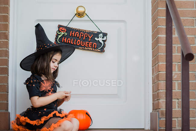 Menina em traje de bruxa com abóbora sobre a porta aberta — Fotografia de Stock