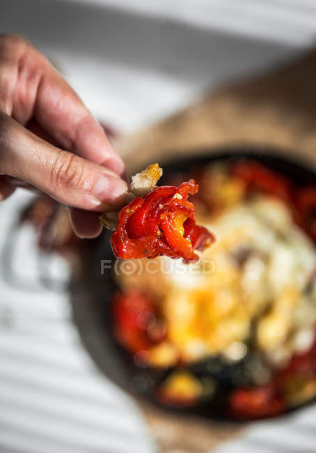 Above view of hand holding dried tomato over pan with scrambled eggs — Stock Photo