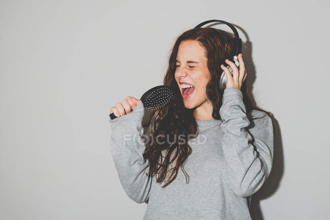 Mulher em fones de ouvido cantando em escova de cabelo — Fotografia de Stock