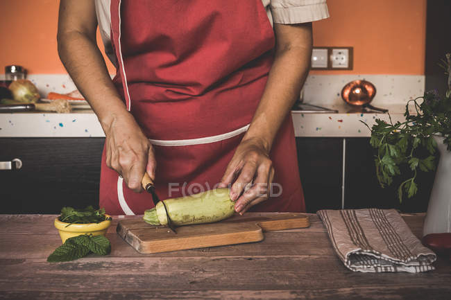 Midsection of woman slicing marrow squash on wooden board — Stock Photo