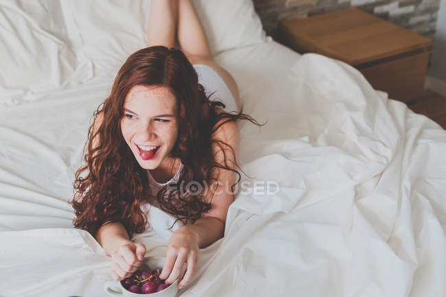 Женщина в нижнем белье ест виноград на кровати — стоковое фото