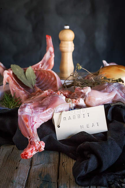 Carcaça de coelho cru com ingredientes e etiqueta na mesa de madeira — Fotografia de Stock
