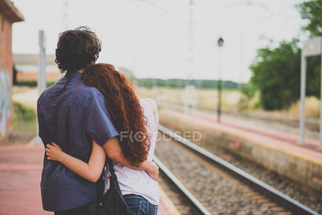 Вид сзади на обнимающую пару молодых людей на сельской железнодорожной платформе — стоковое фото