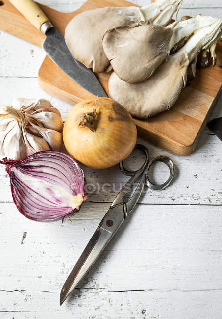 Close up view of board with pleurotus mushrooms and rural knife on rustic table with onion and garlic — Stock Photo