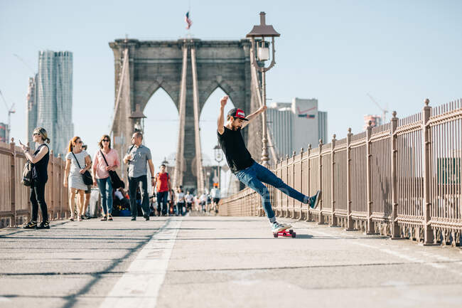 Um jovem fazendo truques e mantém seu equilíbrio no skate na ponte — Fotografia de Stock