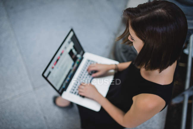Alto ángulo retrato de chica morena usando el ordenador portátil en sus rodillas - foto de stock
