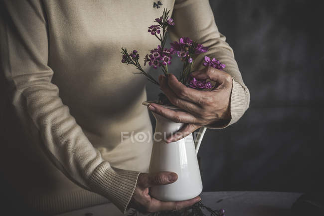 Nahaufnahme weiblicher Hände, die eine Vase mit einem Zweig rosa Blumen halten — Stockfoto