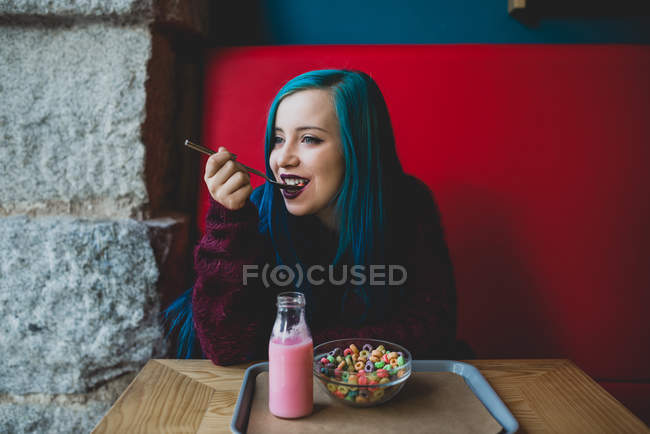 Portrait de fille aux cheveux bleus mangeant des céréales colorées à table de café — Photo de stock