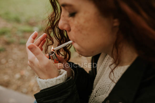 Рыжая девушка с веснушками, закуривающая сигарету — стоковое фото