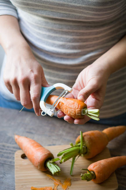 Crop hands  peeling carrot with vegetable pillar — Stock Photo
