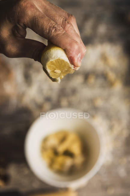 Acima vista de mão espremendo limão em tigela de cerâmica com massa — Fotografia de Stock