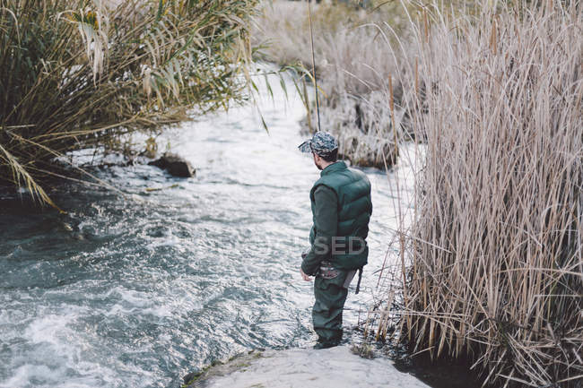 Вид сзади на рыбака, стоящего на берегу и смотрящего на реку — стоковое фото