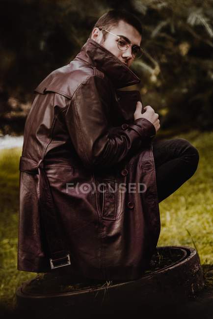 Retrato de homem de casaco de couro agachando no esgoto bueiro e olhando sobre o ombro para a câmera — Fotografia de Stock
