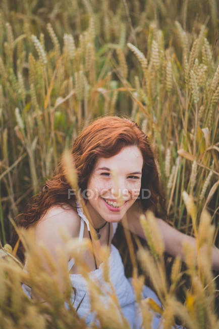 Portrait of happy red head smiling girl sitting in rye and looking at camera — Stock Photo