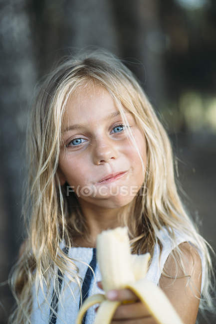 Petite fille mangeant de la banane en plein air et regardant la caméra — Photo de stock