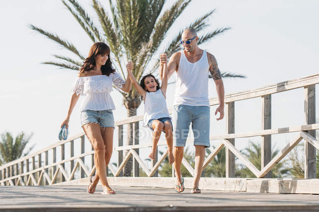 Famiglia passeggiando lungo il ponte e tirando bambina in aria — Foto stock