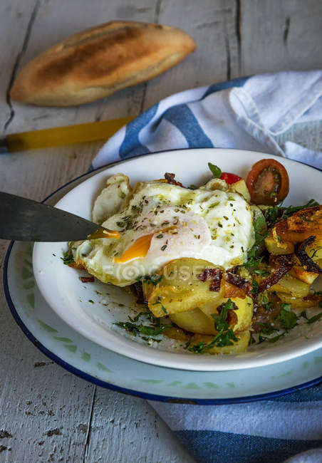 Crop knife slicing fried egg with potatoes in ceramic plate on rural table — Stock Photo