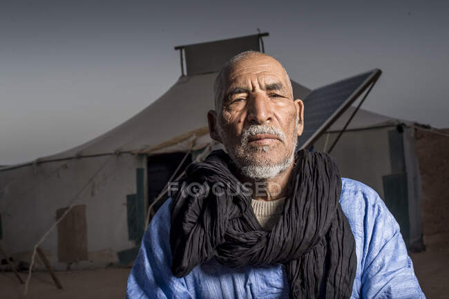 Retrato de árabe mayor y mirando a la cámara sobre la tienda de campaña en el fondo - foto de stock