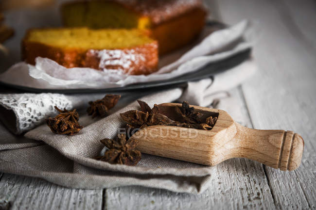 Close up view of wooden scoop of anise stars on towel over homemade cake on background — Stock Photo