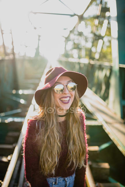 Дівчина в сонцезахисних окулярах сміється на залізничному мосту . — стокове фото