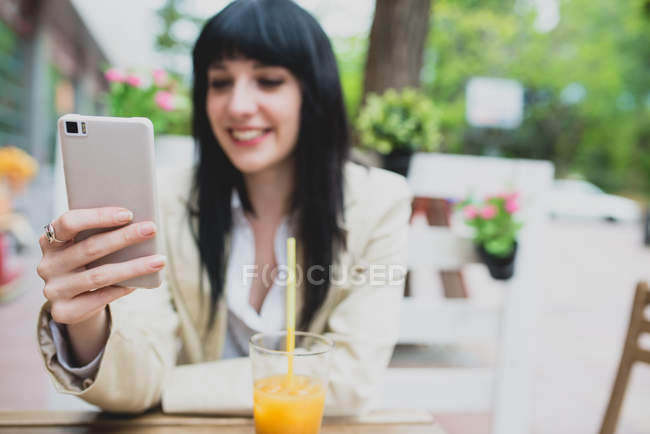 Mulher morena usando mesa de terraço de café smartphone — Fotografia de Stock