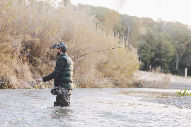 Вид сбоку человека, ловящего рыбу на деревенской реке — стоковое фото