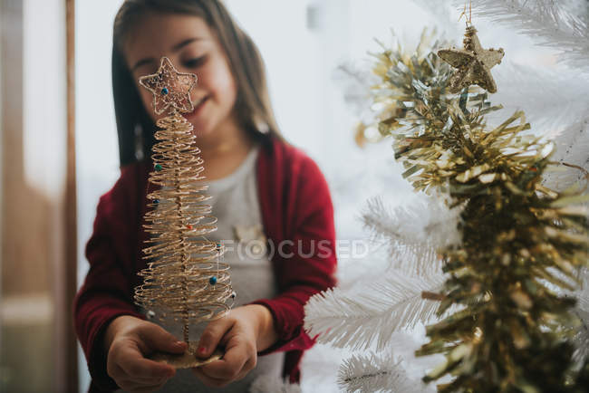 Retrato de una niña sonriente sosteniendo un pequeño árbol de Navidad dorado decorativo - foto de stock