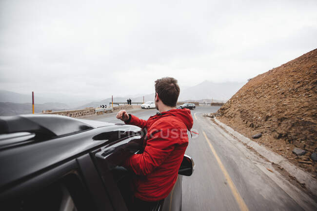 Maschio indossa giacca rossa guardando fuori dal finestrino dell'auto e guardando in lontananza. — Foto stock