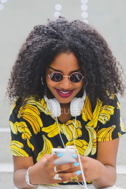 Портрет веселой женщины в солнцезащитных очках, сидящей на лестнице и использующей смартфон — стоковое фото