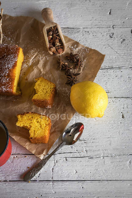 Still life of lemon cake slices with spices and lemon on bakery paper over rural wooden tabel — Stock Photo