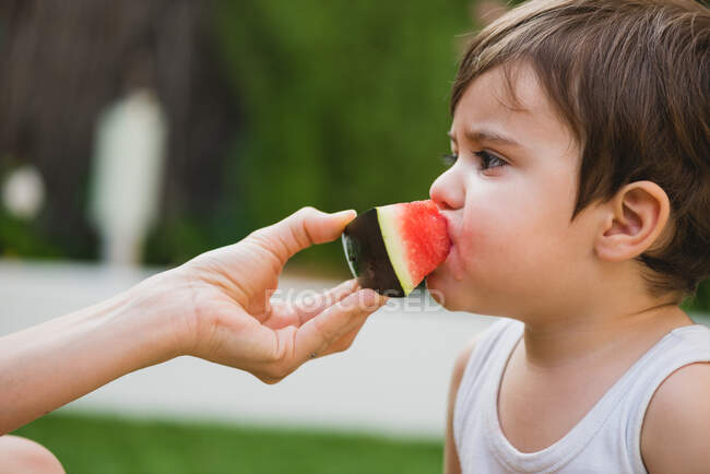 Close-up de mão segurando fatia de melancia enquanto bebê mordendo — Fotografia de Stock