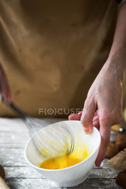 Close-up ver as mãos femininas batendo ovos com batedor em tigela de cerâmica branca — Fotografia de Stock
