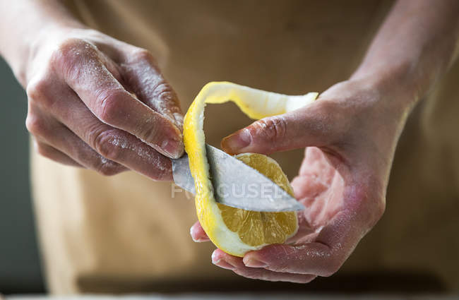 Крупним планом вид жіночих рук, що відрізають лимонну шкірку ножем — стокове фото