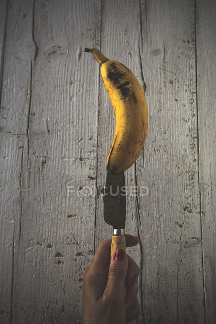 Close-up of female hand holding knife with half of fresh banana — Stock Photo