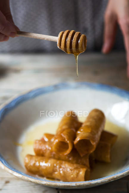 Close up view of female hand pouring honey on fried honey dough tubes with honey spoon — Stock Photo