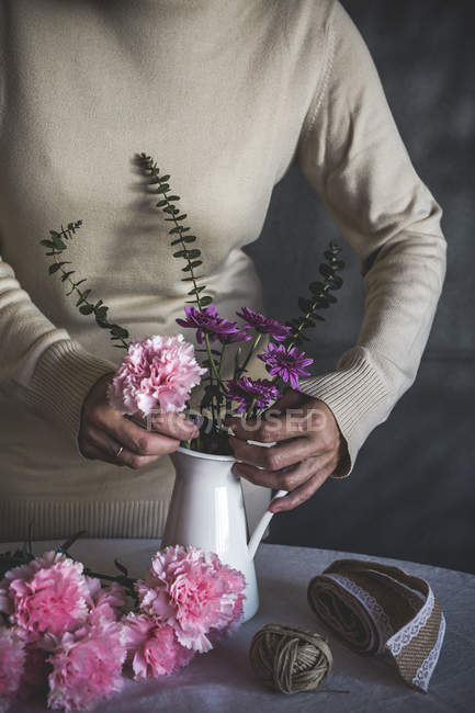 Sezione centrale di fiorista femminile che mette il fiore in vaso su tavolo — Foto stock