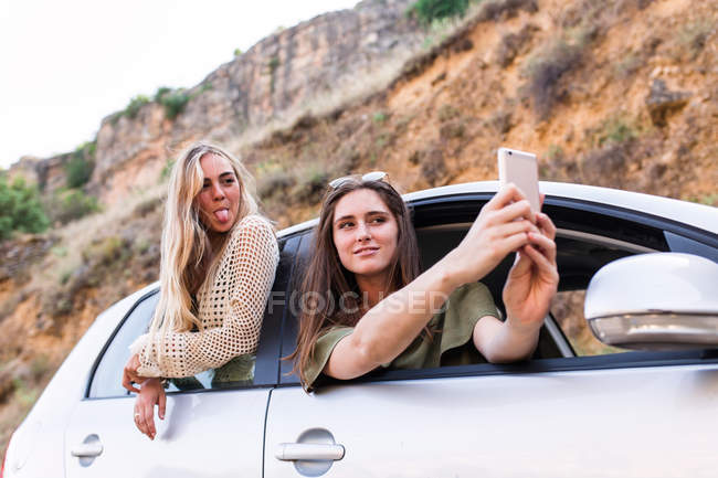 Freunde schauen aus dem Autofenster und machen Selfie — Stockfoto