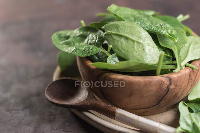 Close up view of wooden bowl with spinach leaves with rustic wooden spoon on table — Stock Photo