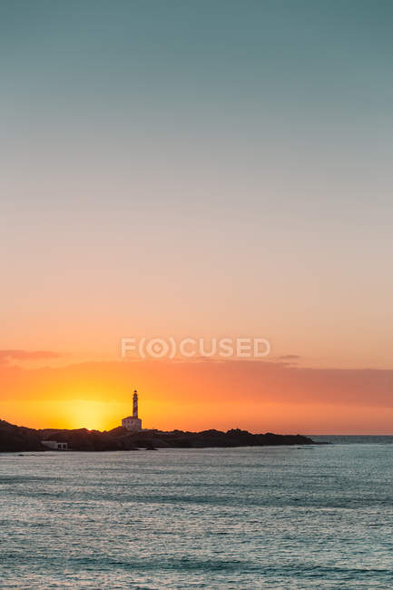 Sunset seascape with lighthouse silhouette on coastline — Stock Photo